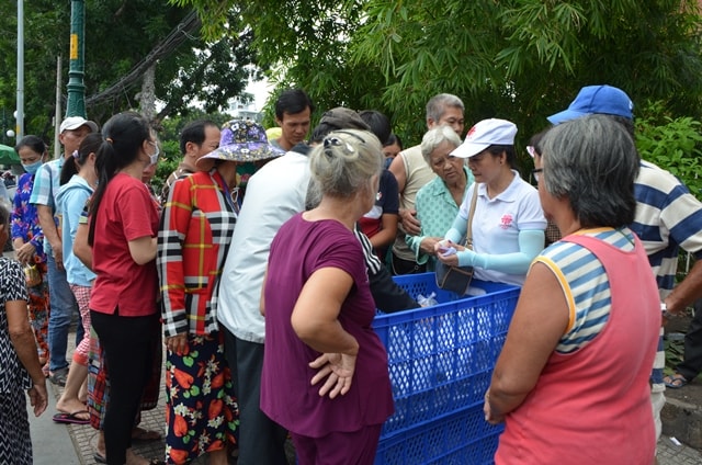 Thành viên của các nhóm từ thiện vừa nhận phiếu vừa phát cơm cho người nhà và bệnh nhân tại cổng bệnh viện Nhân dân 115 TP. HCM.