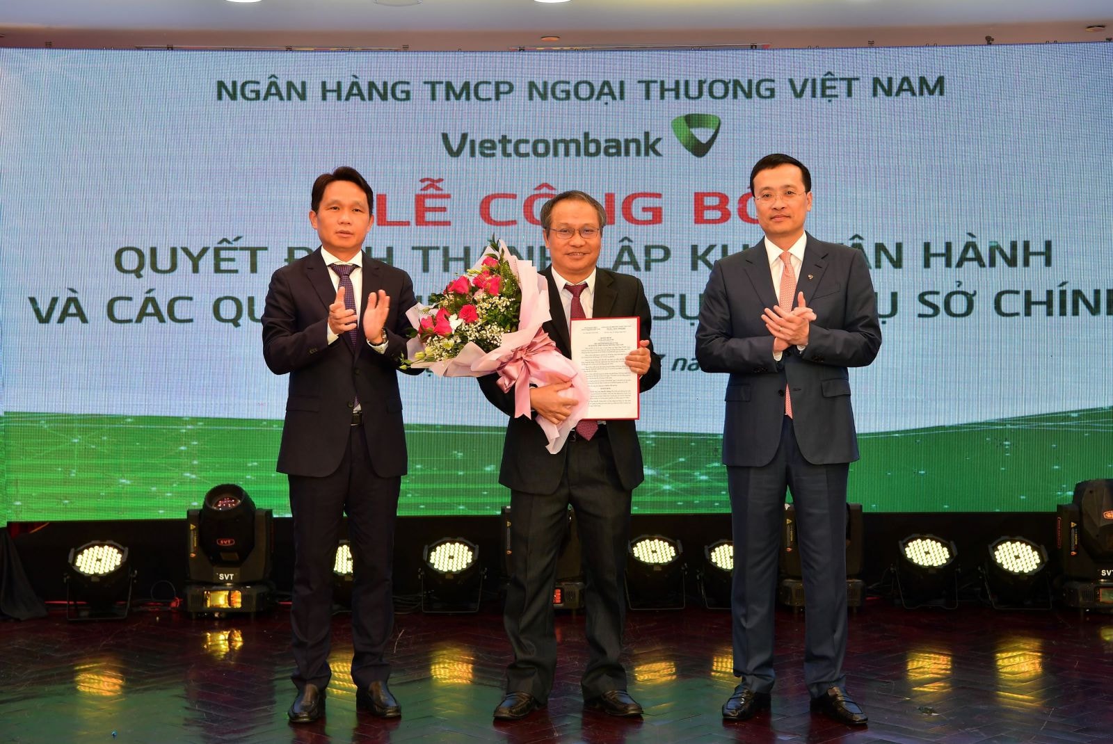 Ông Phạm Quang Dũng - Chủ tịch HĐQT (bên phải) trao quyết định và ông Nguyễn Mạnh Hùng - Thành viên HĐQT tặng hoa chúc mừng tân Trưởng nhóm Nghiên cứu Vietcombank - Tiến sỹ Nguyễn Thắng