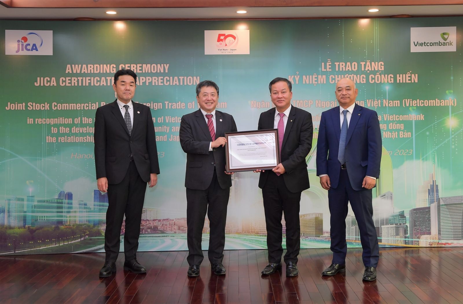 Đại diện Vietcombank, ông Nguyễn Việt Cường - Phó Tổng Giám đốc cùng ông Shojiro Mizoguchi - Thành viên HĐQT, Phó Tổng Giám đốc (thứ 2 và thứ 1 bên phải) nhận Kỷ niệm chương cống hiến do đại diện Văn phòng JICA tại Việt Nam - ông Shimizu Akira, Trưởng đại diện trao tặng