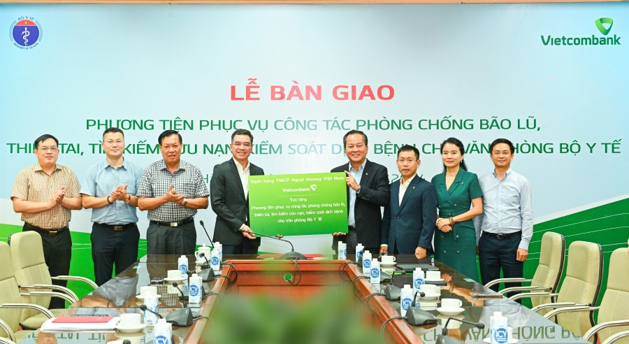 Đại diện Vietcombank, ông Nguyễn Việt Cường - Phó Tổng Giám đốc (thứ 4 từ phải sang) và đại diện Bộ Y tế, Hà Anh Đức - Chánh Văn phòng Bộ Y tế (thứ 4 từ trái sang) thực hiện nghi thức trao gói ASXH.