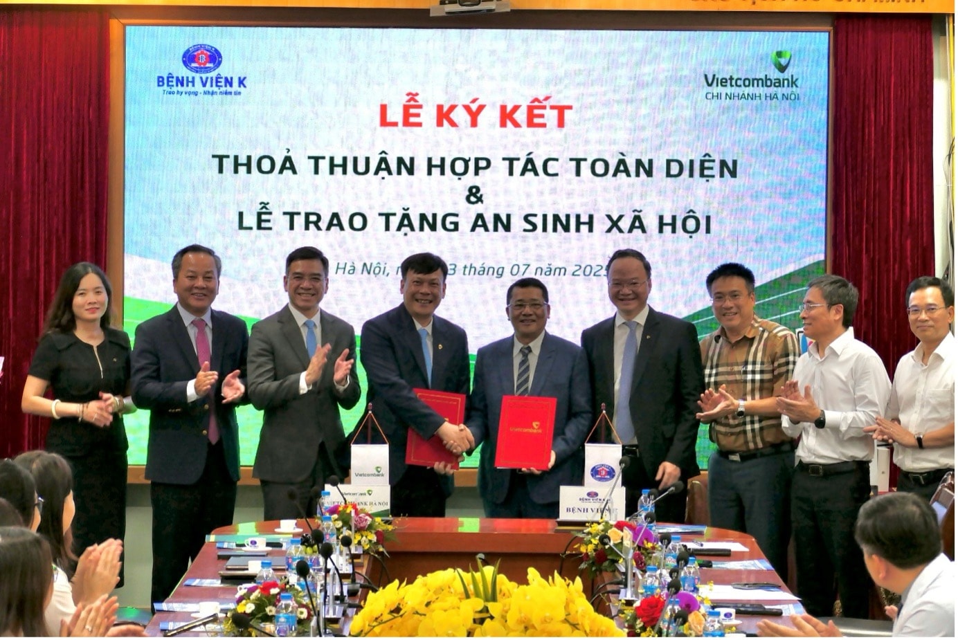 Ông Lê Văn Quảng - Giám đốc Bệnh viện K (thứ 5 phải qua) và ông Lê Ngọc Thái - Giám đốc Vietcombank Hà Nội (thứ 4 từ phải qua) đại diện hai đơn vị hoàn thành nghi thức ký kết thỏa thuận hợp tác trước sự chứng kiến của các đại biểu khách mời.